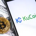 KuCoin open on a smarphone next to a bitcoin and money
